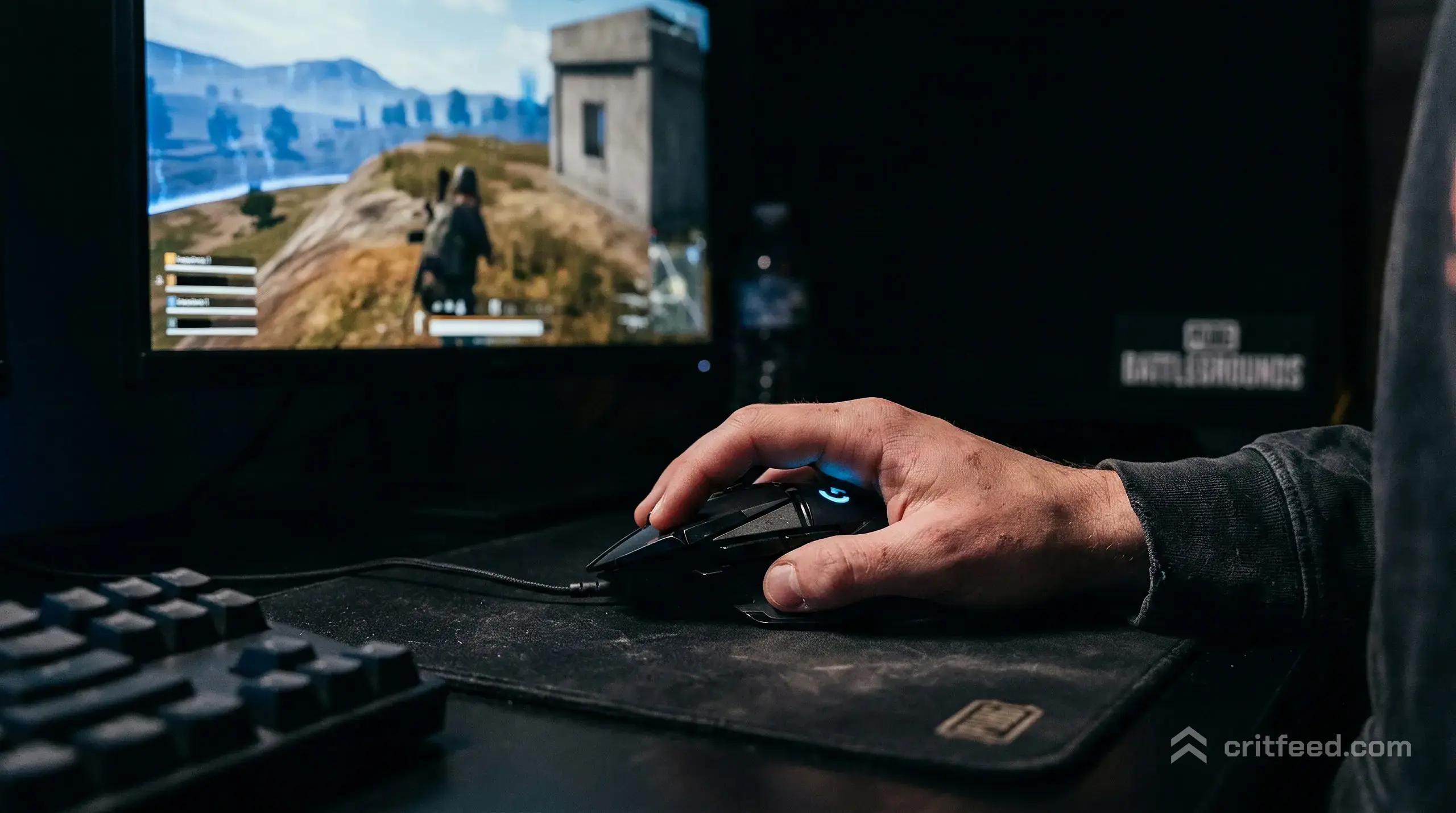 Close-up of a player's right hand on a gaming mouse, side-lit by a single monitor, index finger resting on the main button