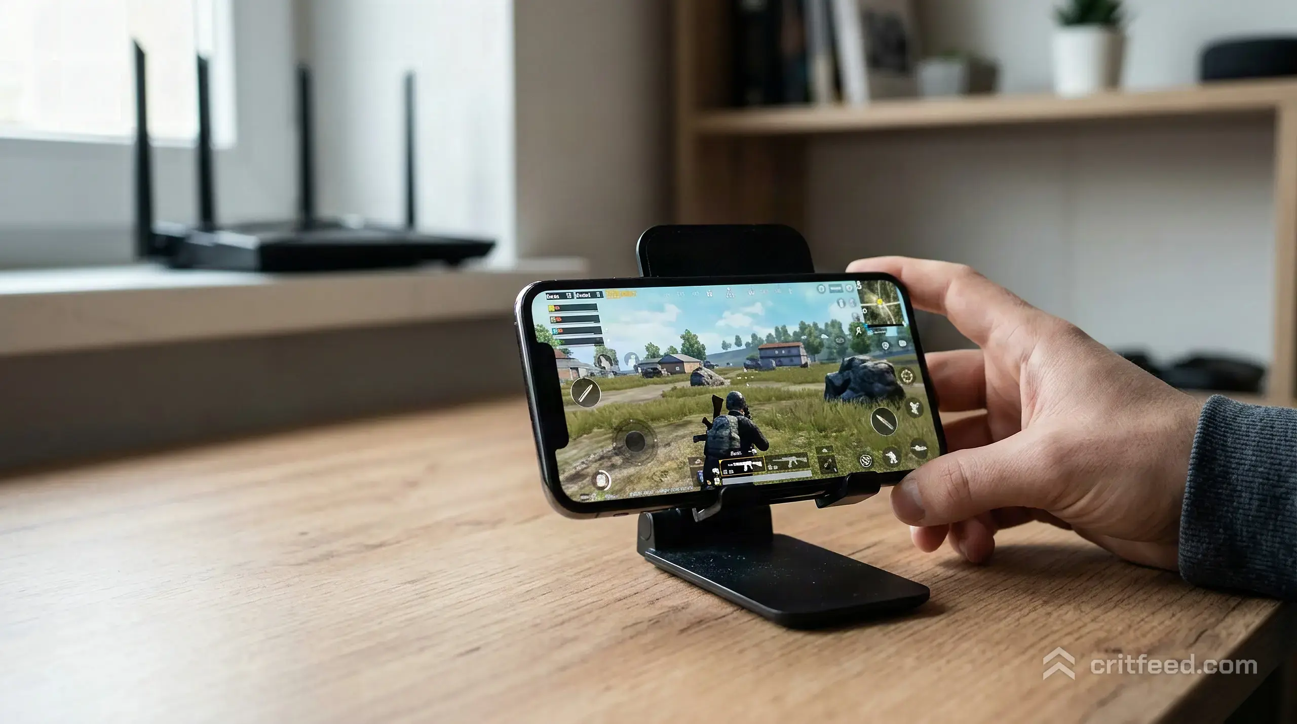 A phone propped on a desk, screen showing a game in progress, a Wi-Fi router out of focus in the background on a shelf