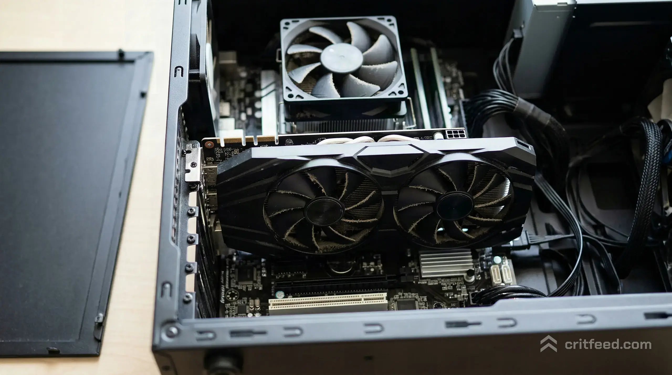 an overhead view of a tower PC's side panel removed, a dual-fan graphics card seated in the slot, dust visible on the fan