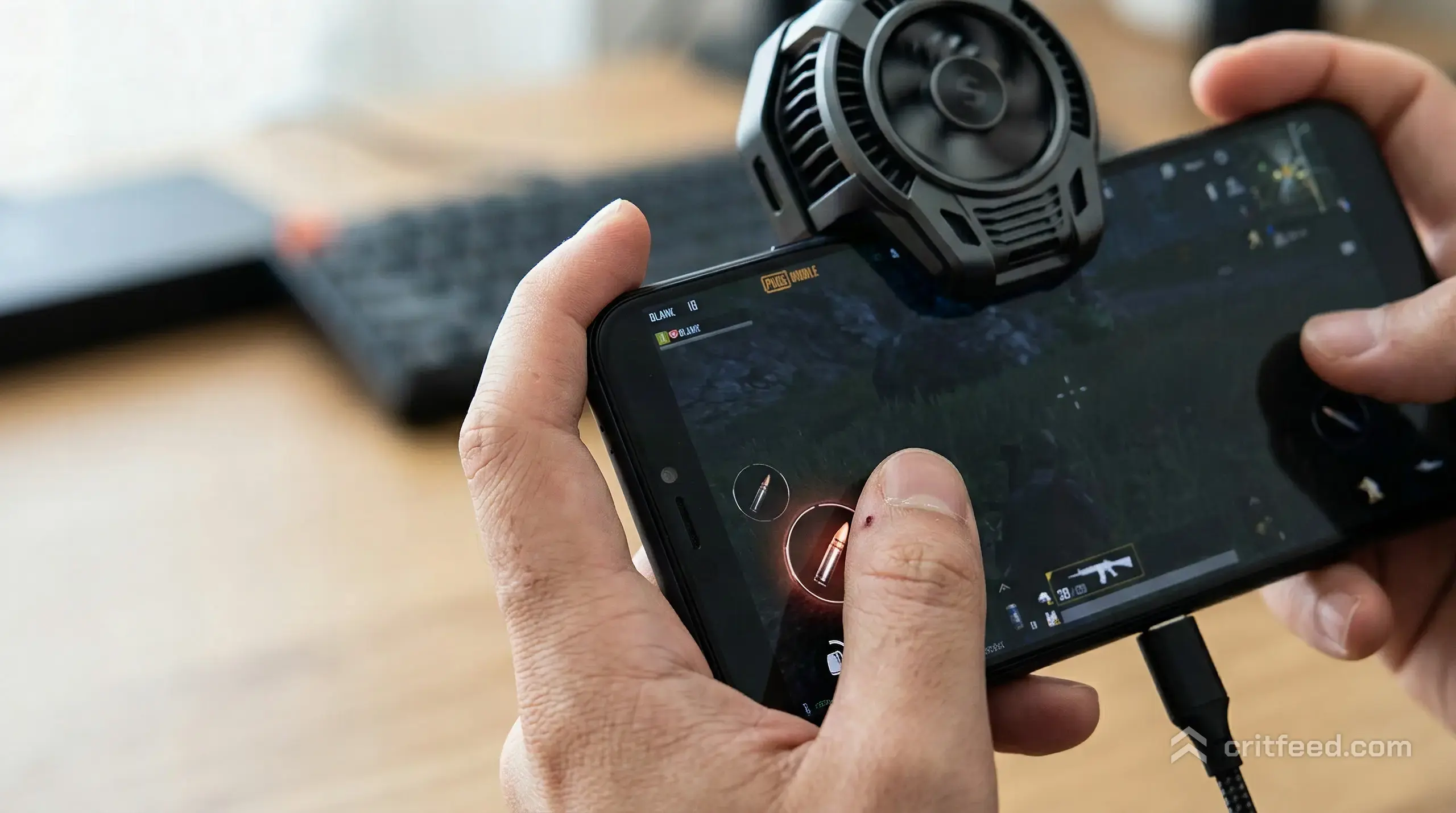 close-up of a thumb resting on the right-side fire button of a dark phone screen, the HUD glowing faintly at the edges, a
