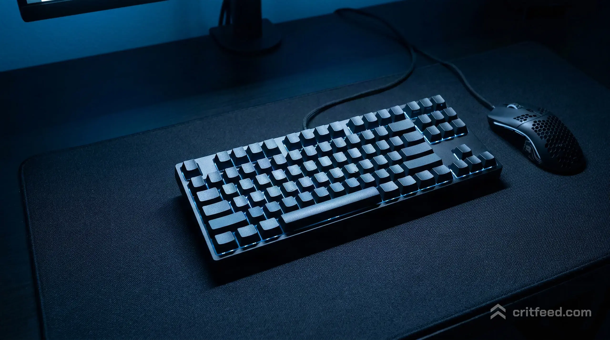 a close overhead shot of a mechanical keyboard and a lightweight gaming mouse on a dark cloth mousepad, lit by the cool blue