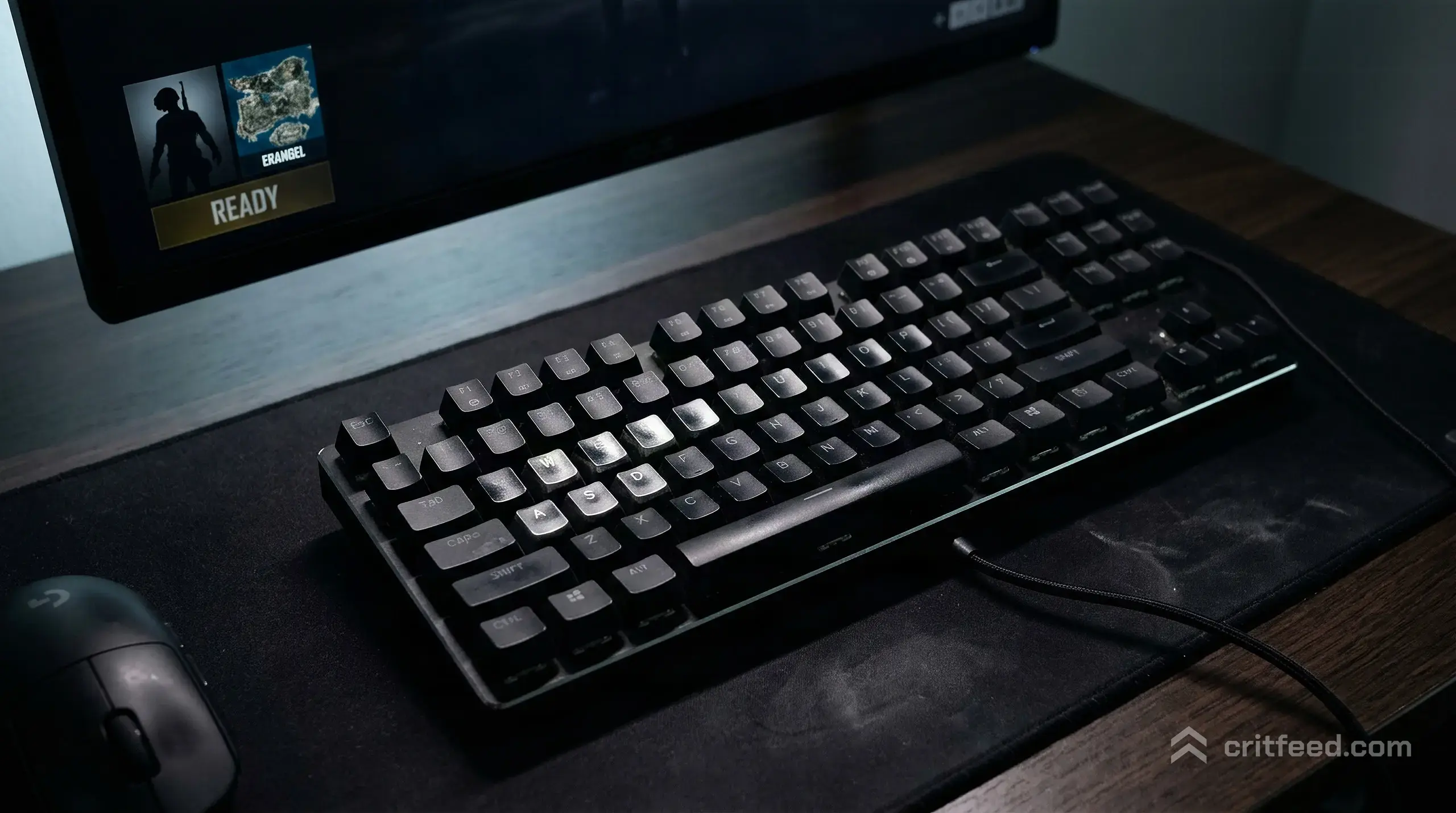 a close overhead shot of a mechanical keyboard with worn WASD keycaps, a dark mousepad, the glow of a single monitor